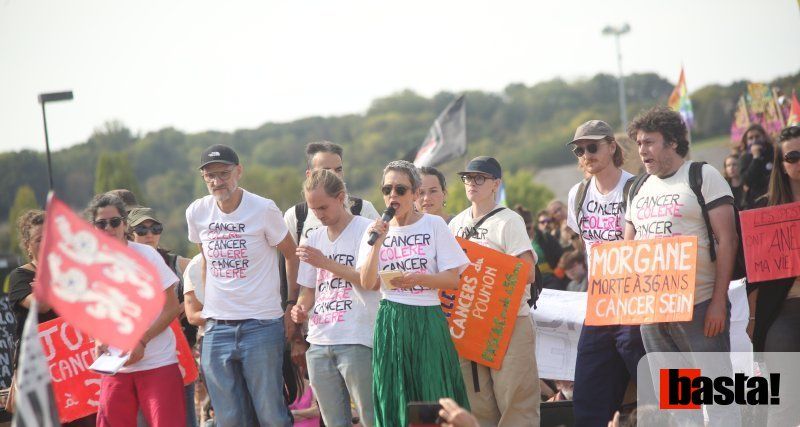 Une femme parle au micro, entourée de manifestant·es en t-shirts « Cancer Colère ».